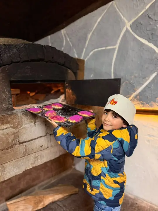 Niño metiendo su charola al horno de leña